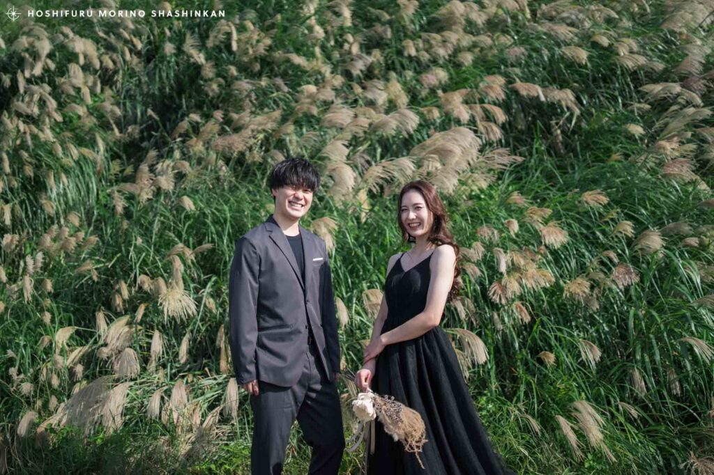 ススキを背景にウインクする新郎と笑顔の新婦